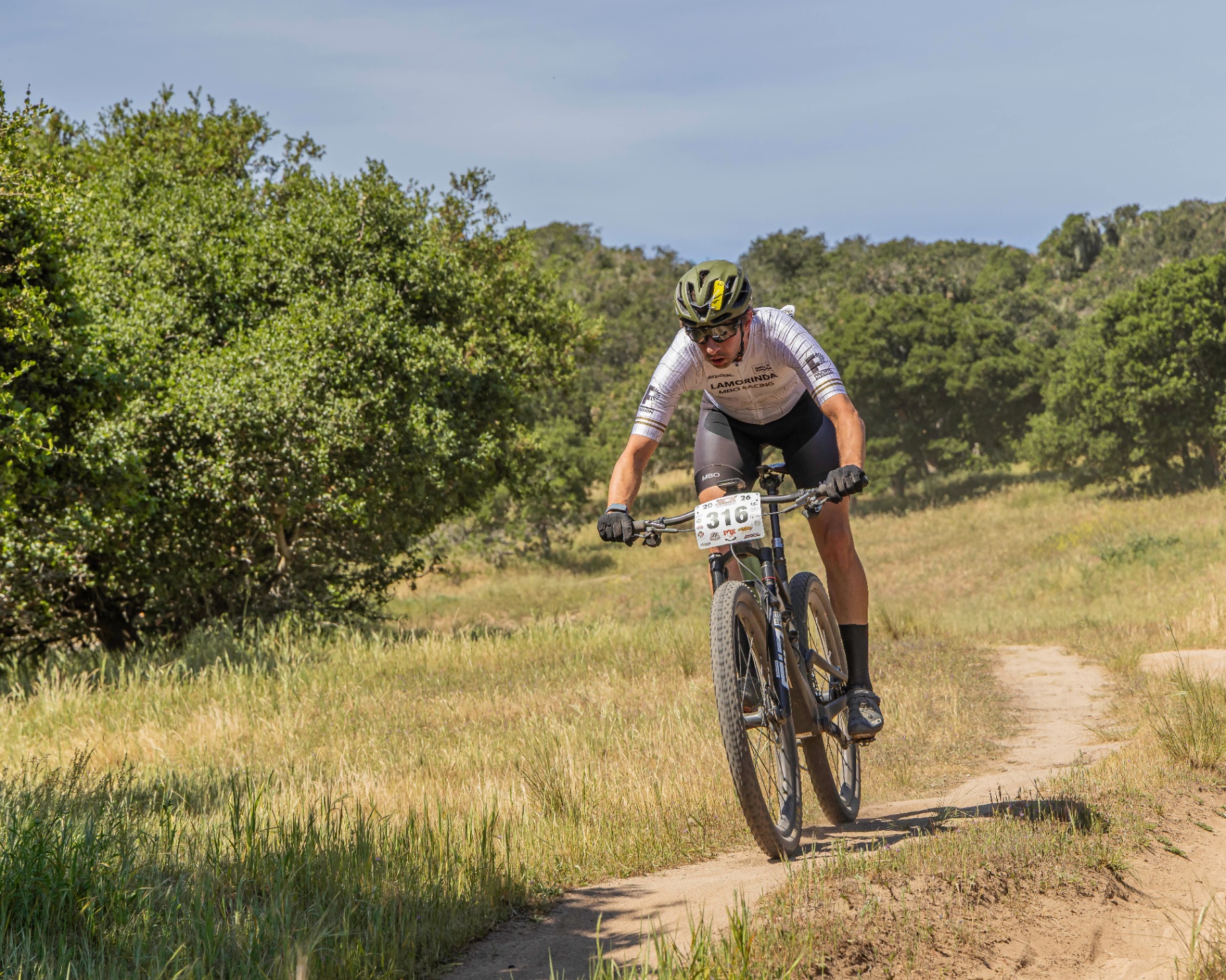 Mountain biker racing hard on a singletrack trail through golden California grasslands