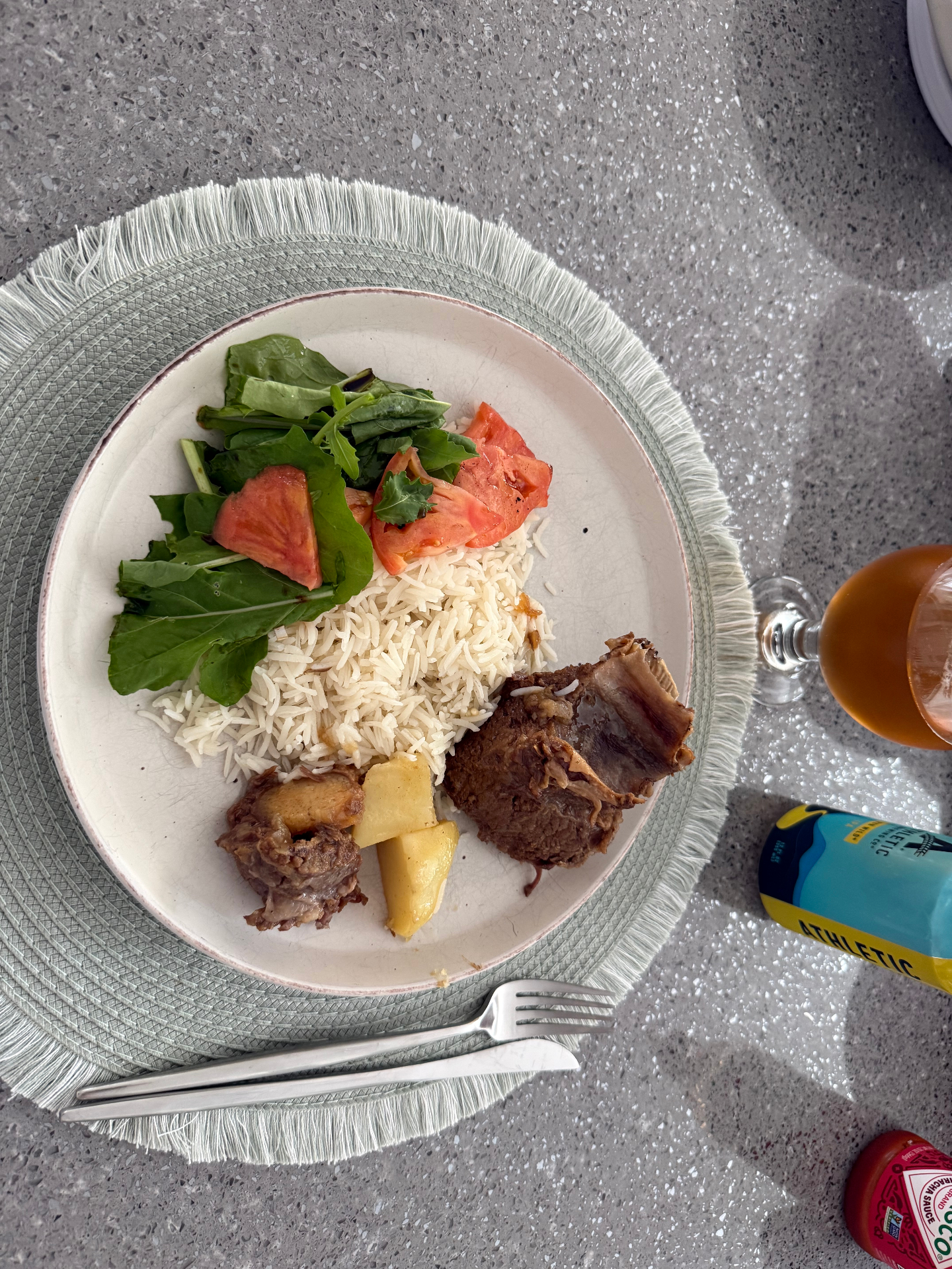 Post-ride recovery plate with basmati rice, slow-cooked beef, roasted potato, arugula and tomato salad, next to a non-alcoholic recovery drink