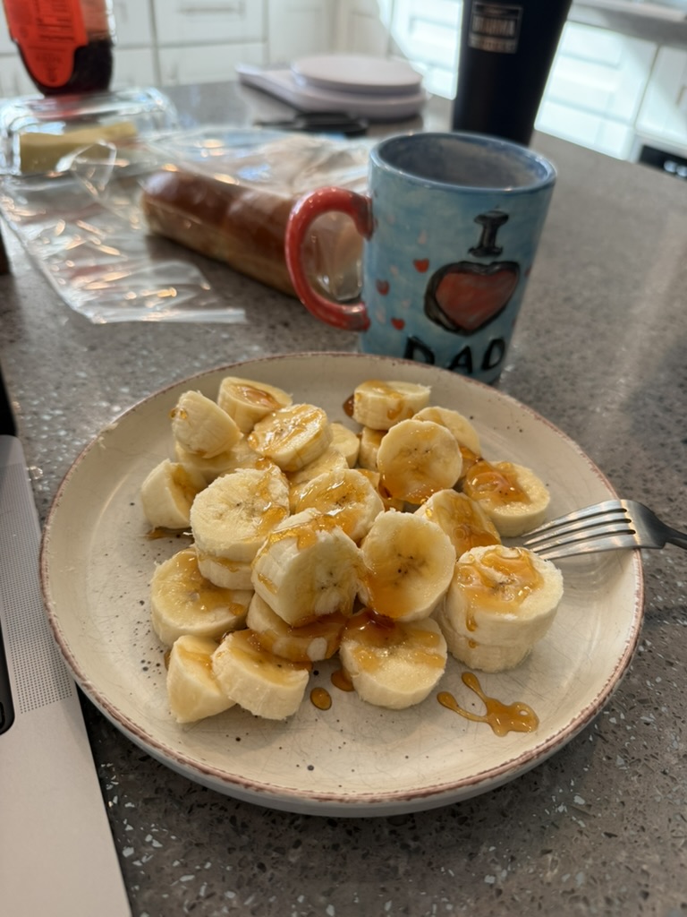 Plate of sliced banana drizzled with honey next to a coffee mug — a simple, carbohydrate-rich pre-race breakfast